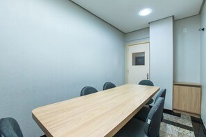 Une salle de conférence avec une table en bois, quatre chaises, une porte et un petit meuble.