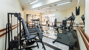 A gym with exercise equipment, a ceiling fan, and large windows. - Hotel Suárez São Leopoldo (Sao Leopoldo)
