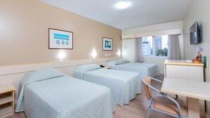 A hotel room with three beds, a desk, a chair, a television, and a window with curtains. - Hotel Suárez São Leopoldo (Sao Leopoldo)