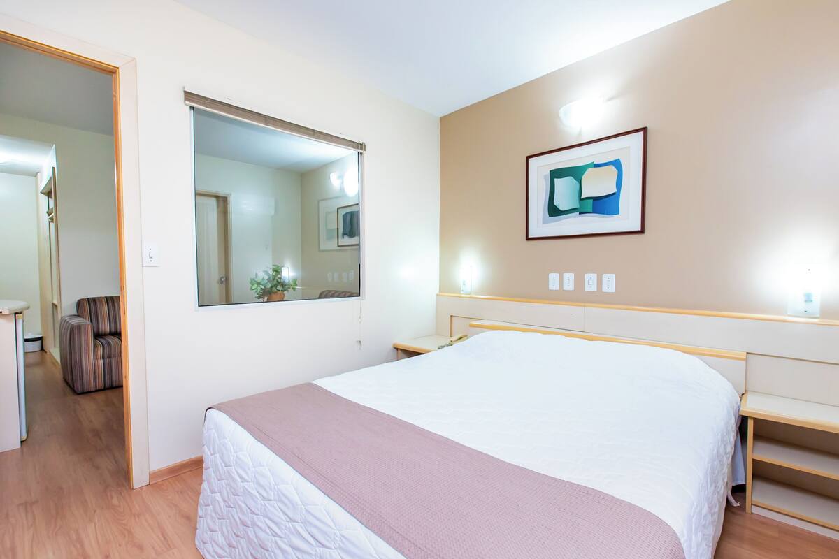 Ein Hotelzimmer mit einem Bett, einem Nachttisch, einem Stuhl, einem Spiegel und einem gerahmten Bild an der Wand.