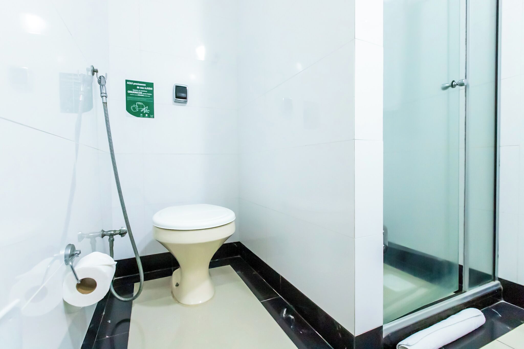 A bathroom with a toilet, a glass shower enclosure, and a towel on the floor.