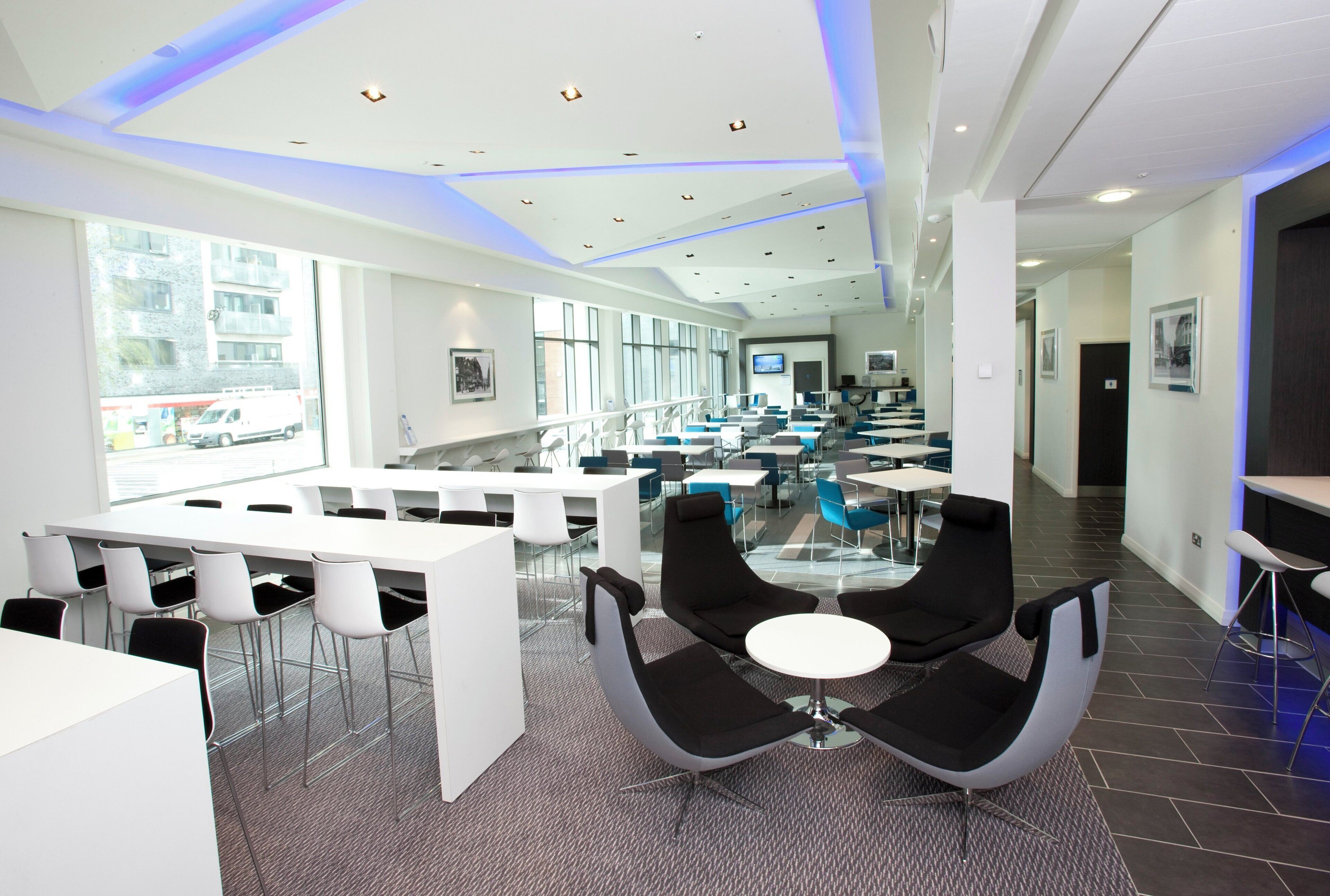 A modern conference room with white tables, black chairs, and a glass partition.
