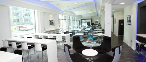 A modern conference room with white tables, black chairs, and a glass partition.
