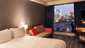 A hotel room with a large bed, a sofa, a desk with a chair, and a large window offering a city view. - Holiday Inn Express Manchester City Centre Arena by IHG (Manchester)
