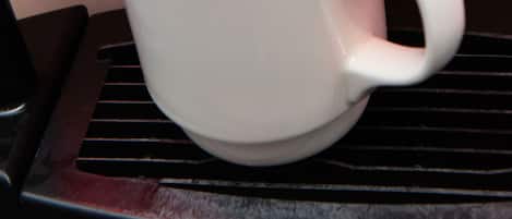 A white cup on a black tray with a coffee machine dispensing coffee into it.
