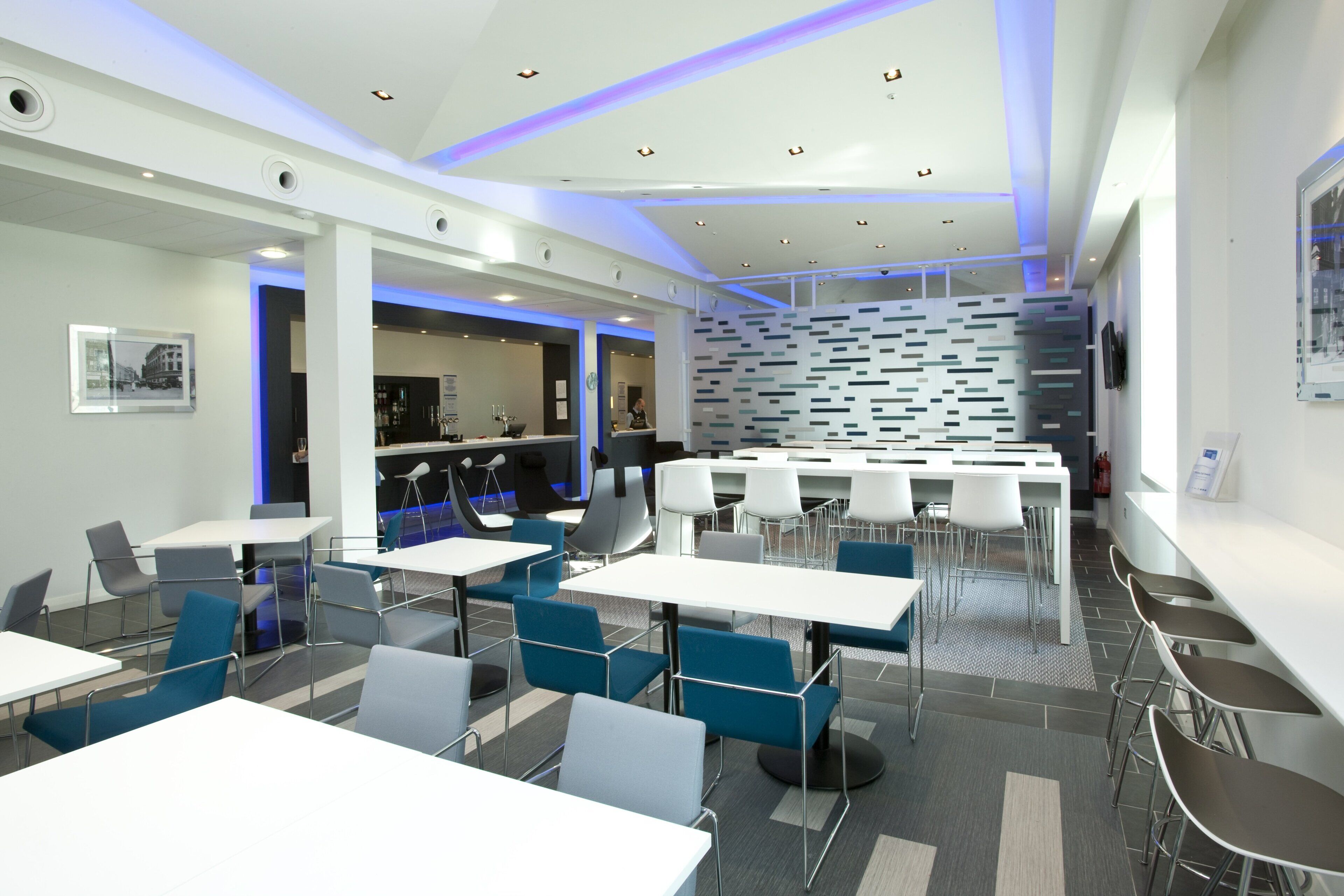 A modern restaurant with white tables and chairs, a bar area, and a patterned wall.