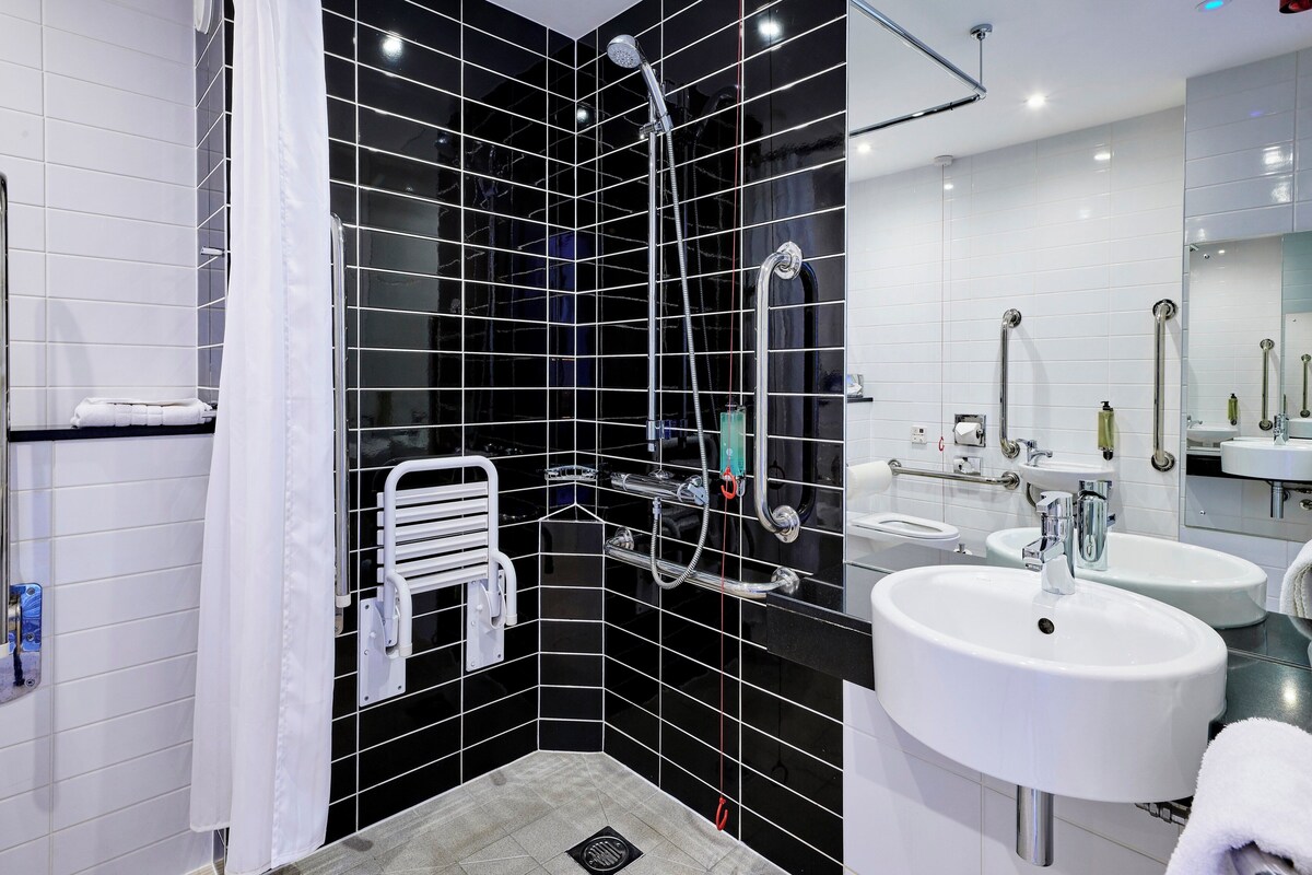 A modern bathroom with black and white tiles, a shower with a handheld showerhead, a towel rack, and two sinks.