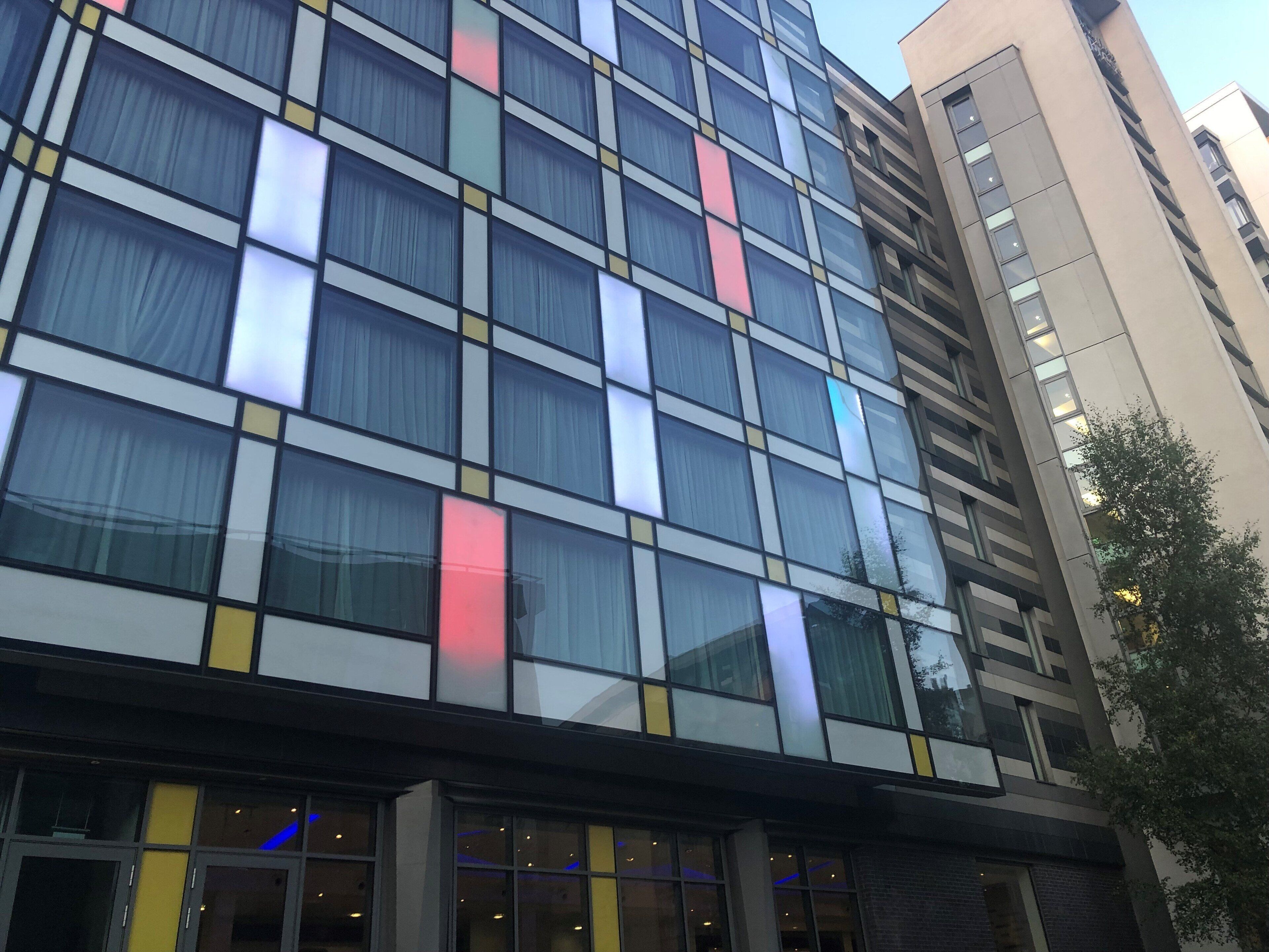 A modern building with a grid of windows, some with colored panels, and a visible entrance with glass doors.