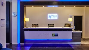 A Holiday Inn Express reception area with a modern design, featuring a reception desk, two lamps, a clock, and a sign indicating the bar opening hours. - Holiday Inn Express Manchester City Centre Arena by IHG (Manchester)