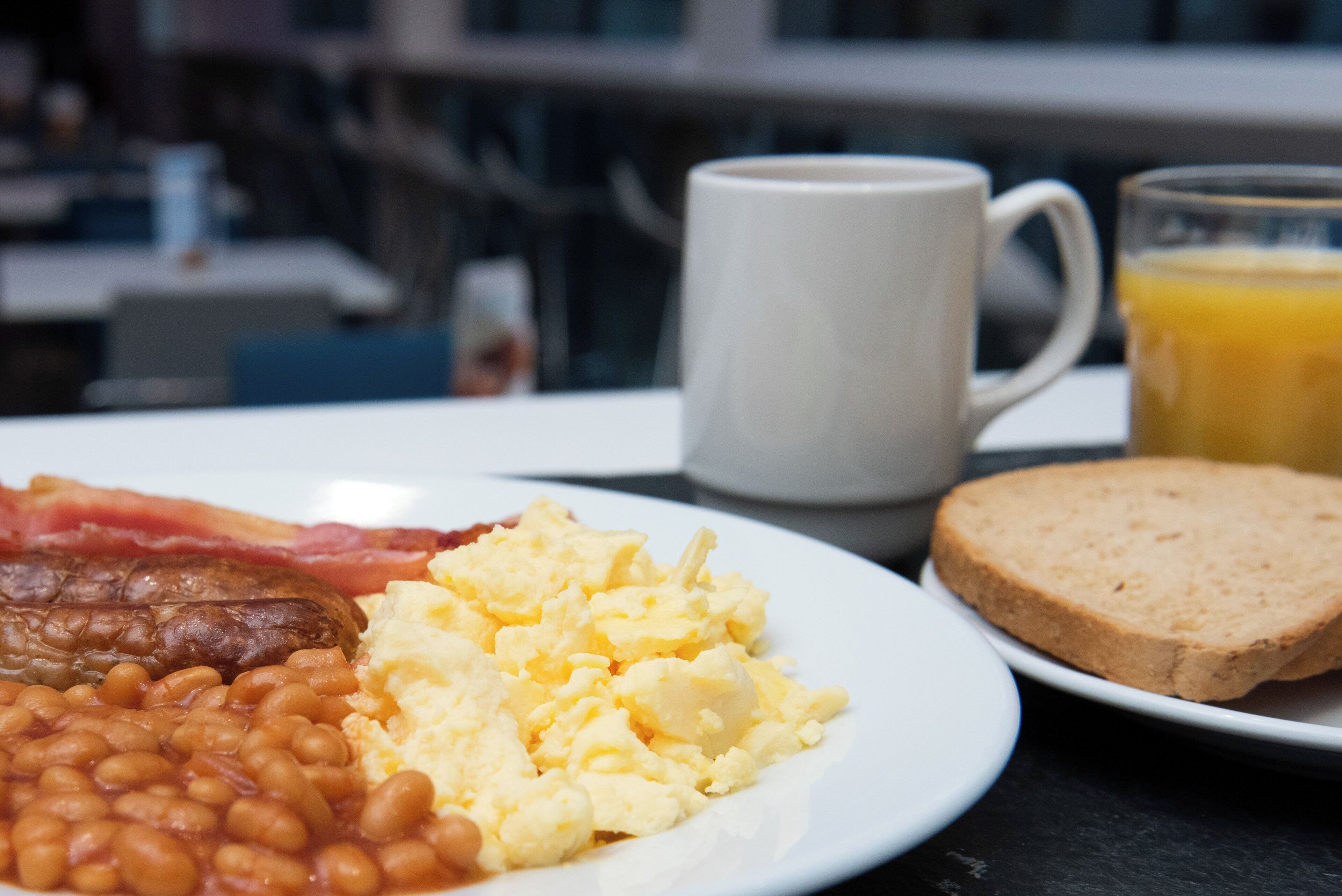 A plate with eggs, bacon, beans, toast, a mug, and a glass of orange juice.