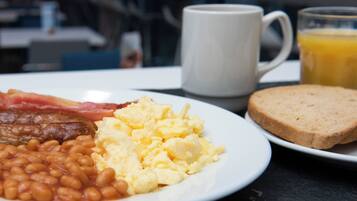 A plate with eggs, bacon, beans, toast, a mug, and a glass of orange juice.