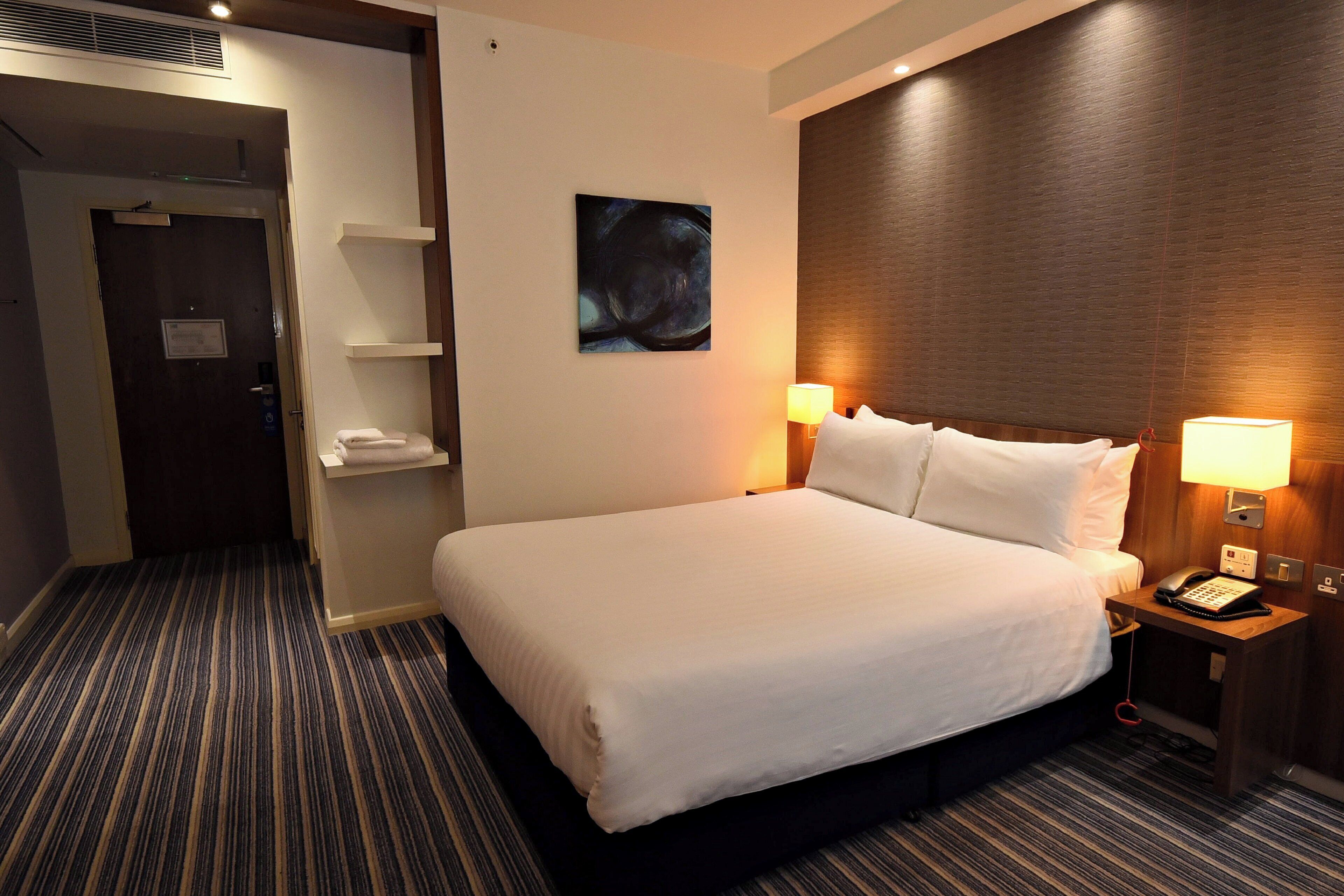 Une chambre d’hôtel avec un grand lit, des lampes de chevet, un téléphone et un tableau au mur.