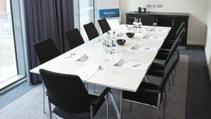 A conference room with a long table, chairs, a whiteboard, a welcome sign, a flat-screen TV, and a window with curtains. - Holiday Inn Express Manchester City Centre Arena by IHG (Manchester)