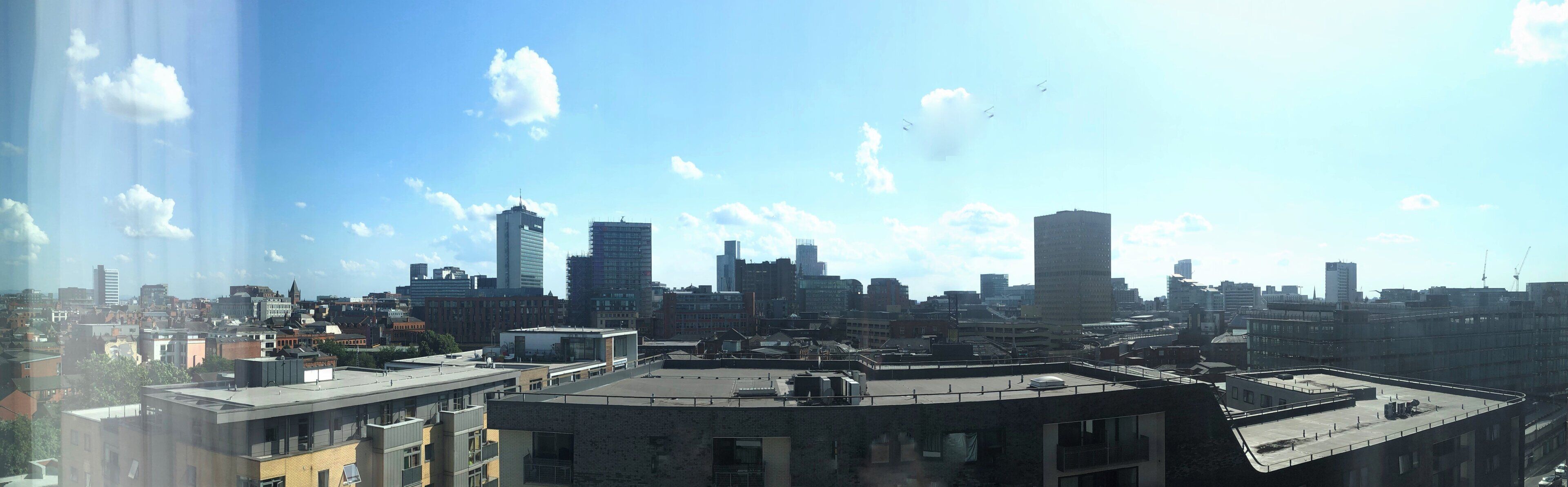 A city skyline with multiple high-rise buildings, a clear sky, and a few clouds.