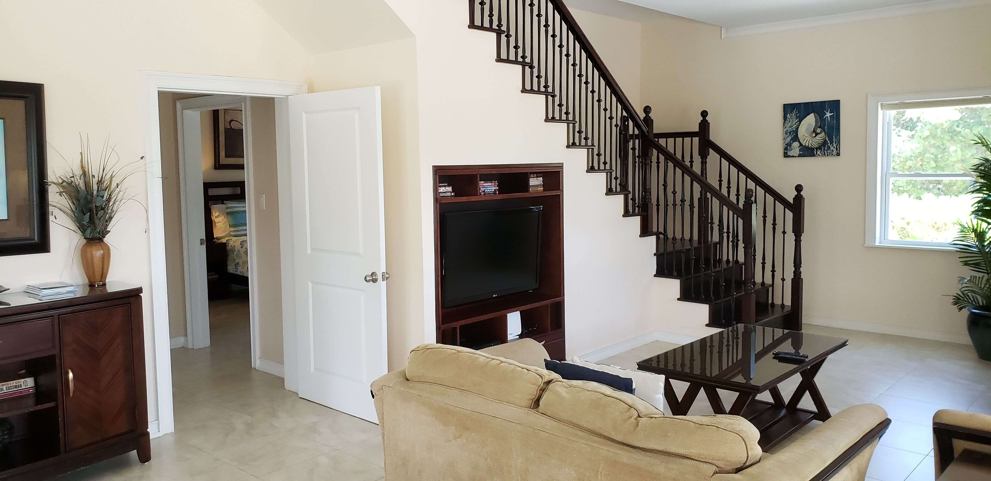 A living room with a beige sofa, a coffee table, a TV stand, and a staircase with a railing.