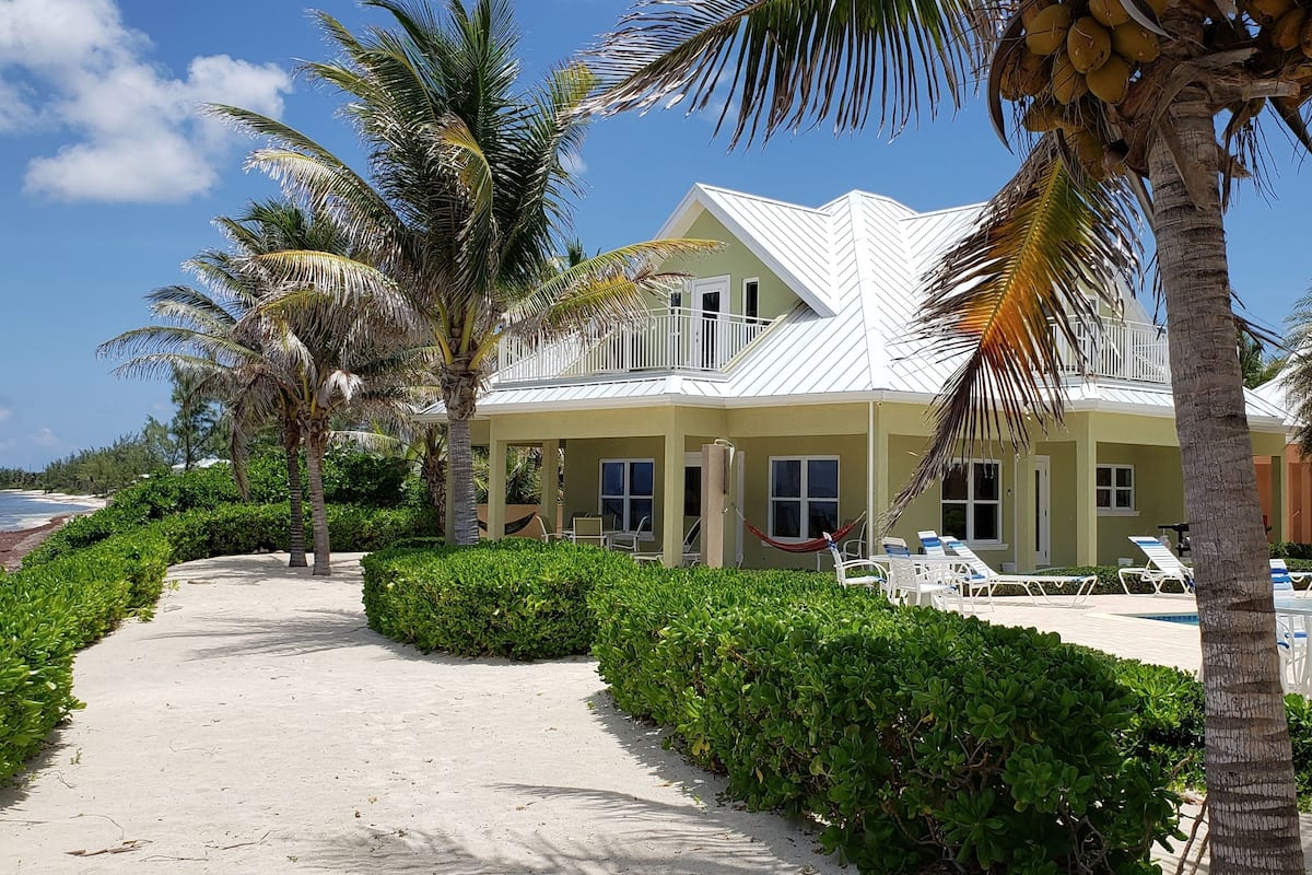A beachfront property with a white-roofed building, a sandy pathway, and palm trees.