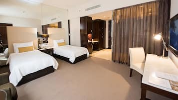 A hotel room with two beds, a desk, a chair, a TV, and a bathroom visible through an open door.
