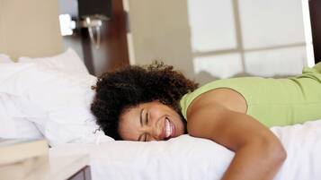 A person lying in bed with white bedding, a green tank top, and a white pillow.