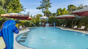 Relax by the serene pool surrounded by lush greenery and tall trees, with lounge chairs and umbrellas for a comfortable stay.
