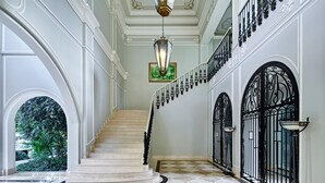 Una imponente escalera con piso de mármol a cuadros, paredes blancas y barandillas de hierro forjado negro.