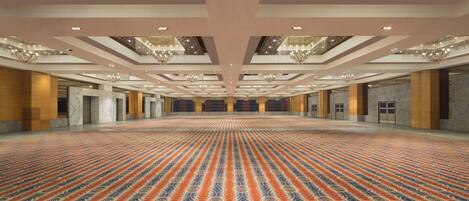 A large, open hall with a patterned carpet, chandeliers, and a high ceiling with a wooden design.