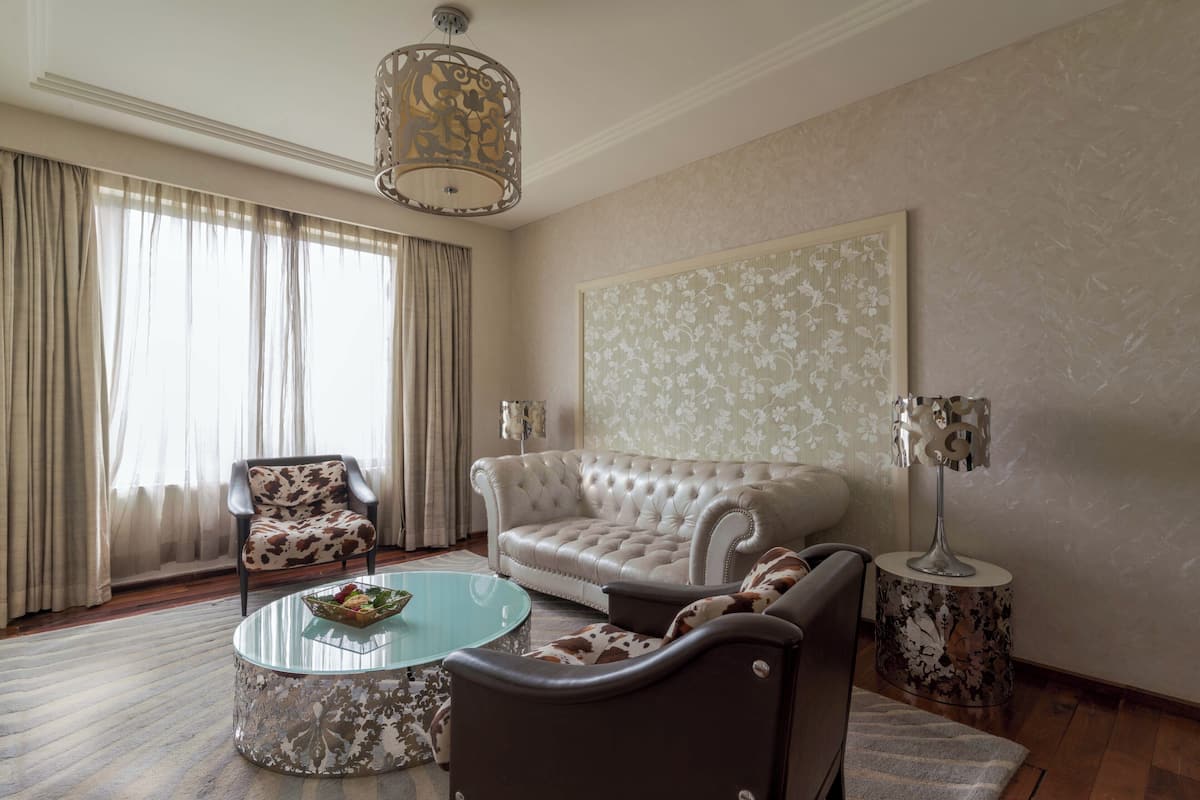 Un salon avec un canapé en cuir, une table basse en verre, un fauteuil à motifs, une lampe sur pied et une grande œuvre d’art florale accrochée au mur.