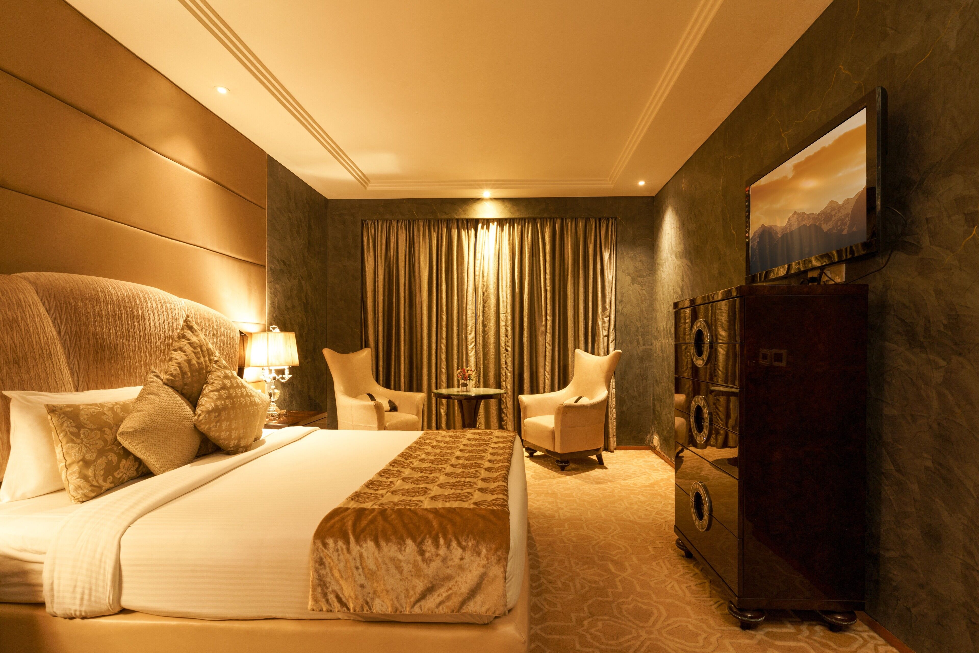 A hotel room with a large bed, two armchairs, a TV, and a minibar.
