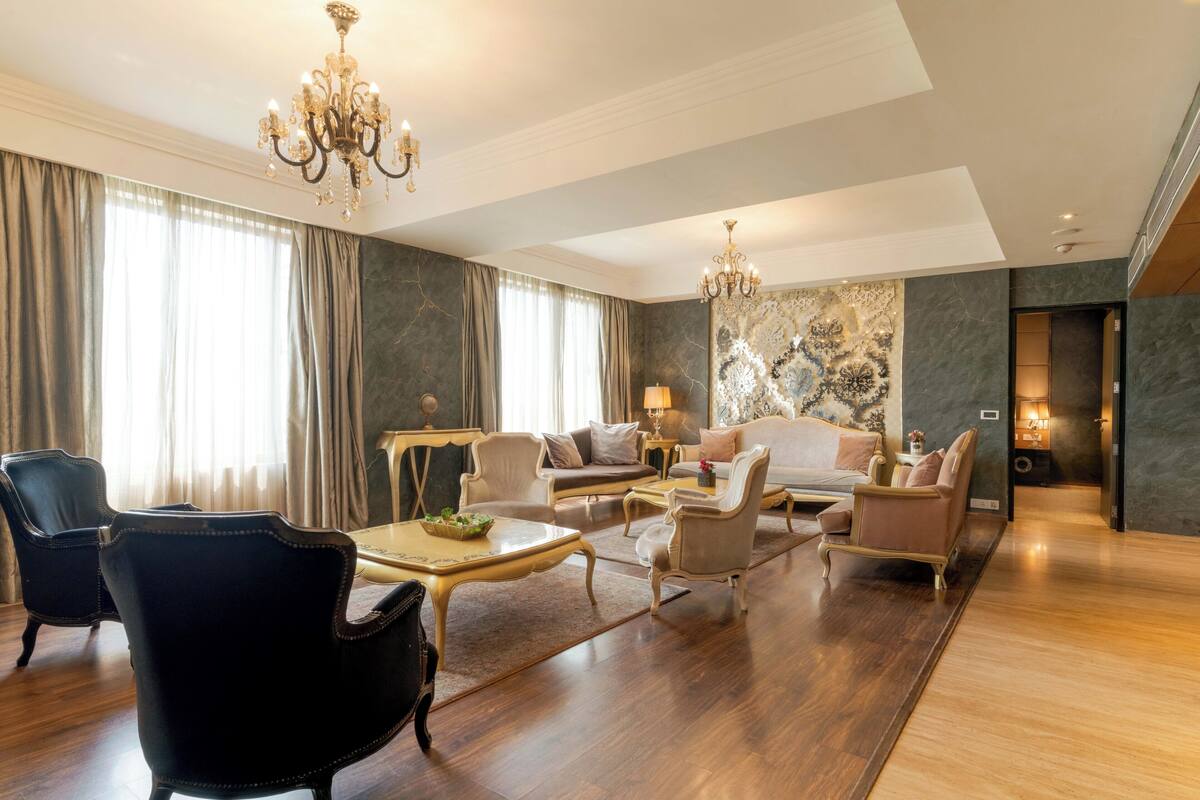 Un salon spacieux agrémenté d’un lustre, de canapés, de fauteuils et d’une table basse.