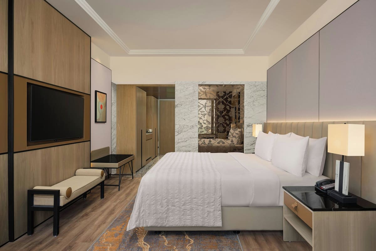 Une chambre d’hôtel moderne, dotée d’un grand lit, d’un bureau, d’une télévision et d’une salle de bain visible à travers une porte ouverte.