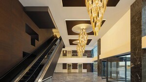 A modern lobby with a marble floor, an escalator, a chandelier, and a glass entrance. - Le Meridien Surat (Surat)