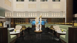 A spacious lobby with seating areas, a central decorative sculpture, and a reception desk. - Le Meridien Surat (Surat)