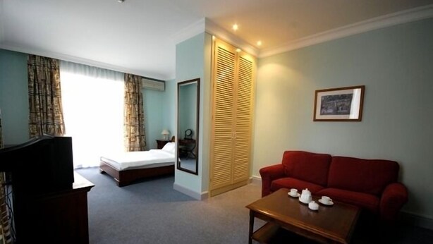 A hotel room with a bed, a red sofa, a wooden coffee table, and a television. - The Horizon Hotel (Baku)