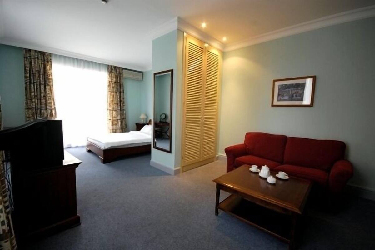 A hotel room with a bed, a red sofa, a wooden coffee table, and a television.