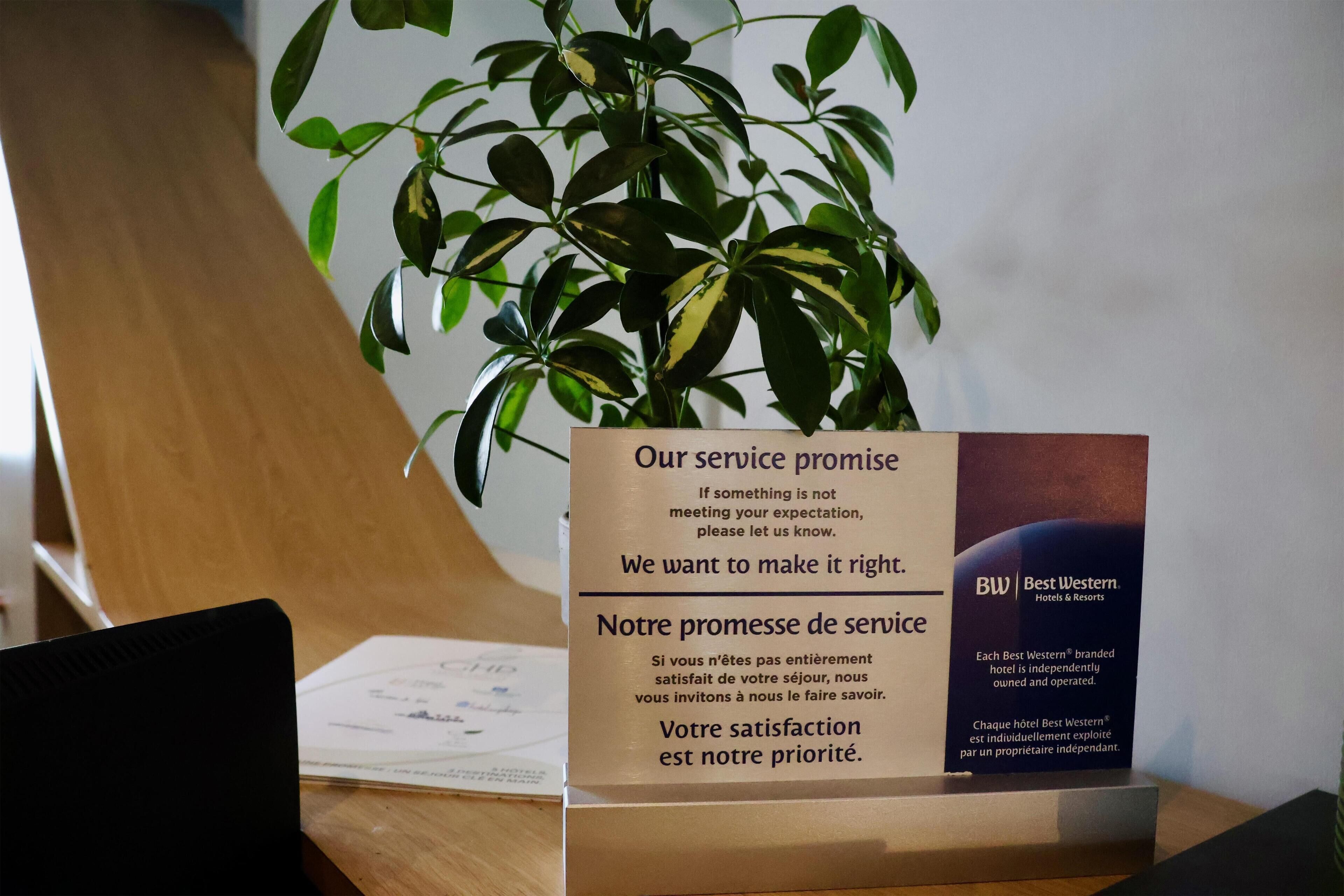 Une enseigne indiquant les engagements de service, avec un texte en anglais et en français, le logo d’un hôtel Best Western et une plante en pot.