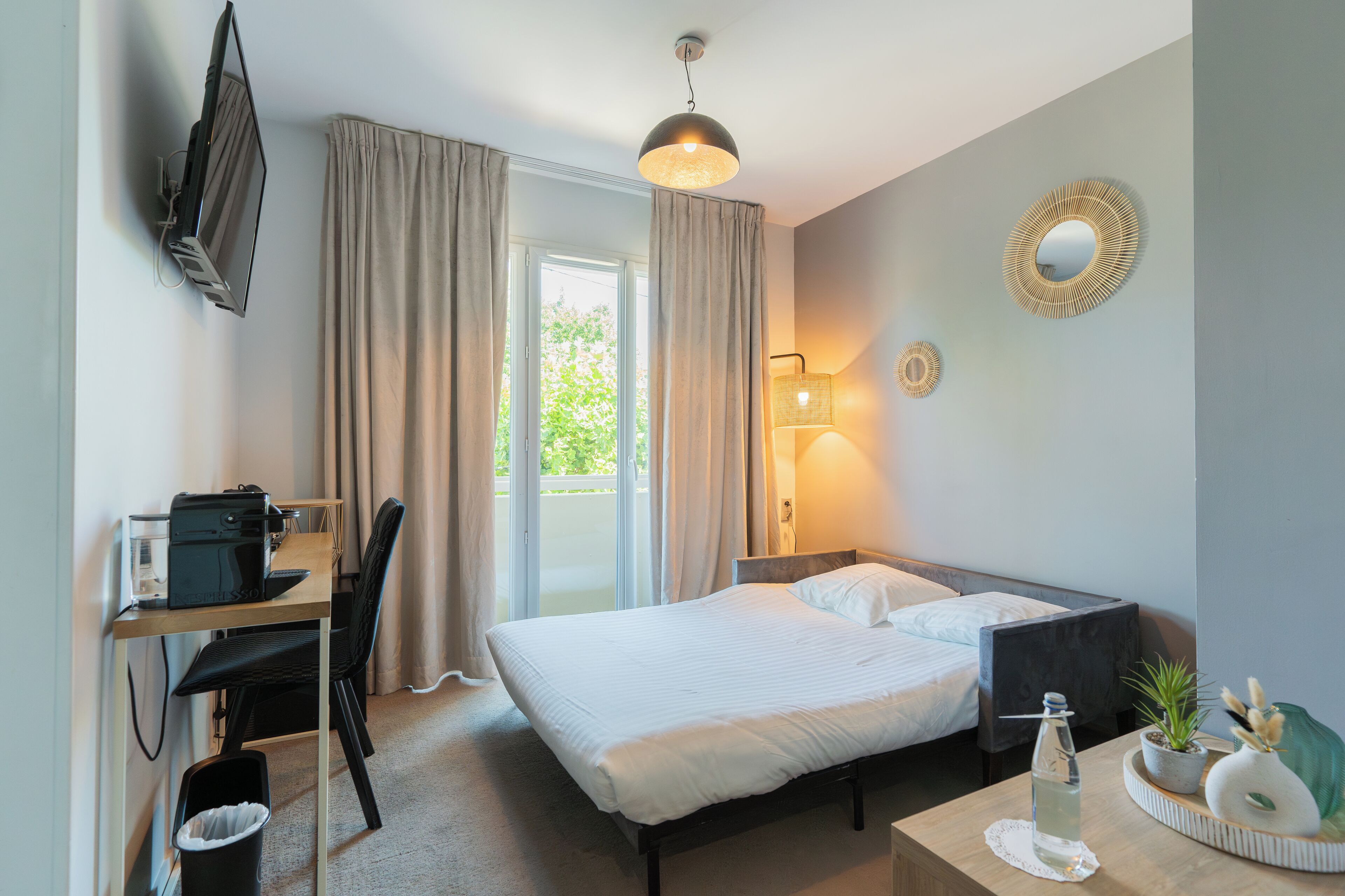 Una habitación de hotel con cama, escritorio, silla y televisor montado en la pared.