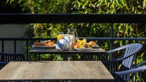 A table with breakfast items, a kettle, and a glass of orange juice on an outdoor balcony with metal railings and greenery in the background. - Best Western Hotel Garden & Spa (La Baule-Escoublac)