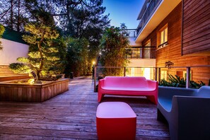 Eine Holzterrasse mit Gartenmöbeln, ein Holzgebäude und ein Garten mit Bäumen.