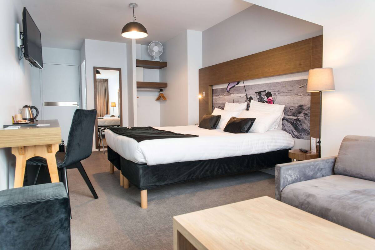 A modern hotel room with a bed, a desk, a chair, a sofa, and a TV.