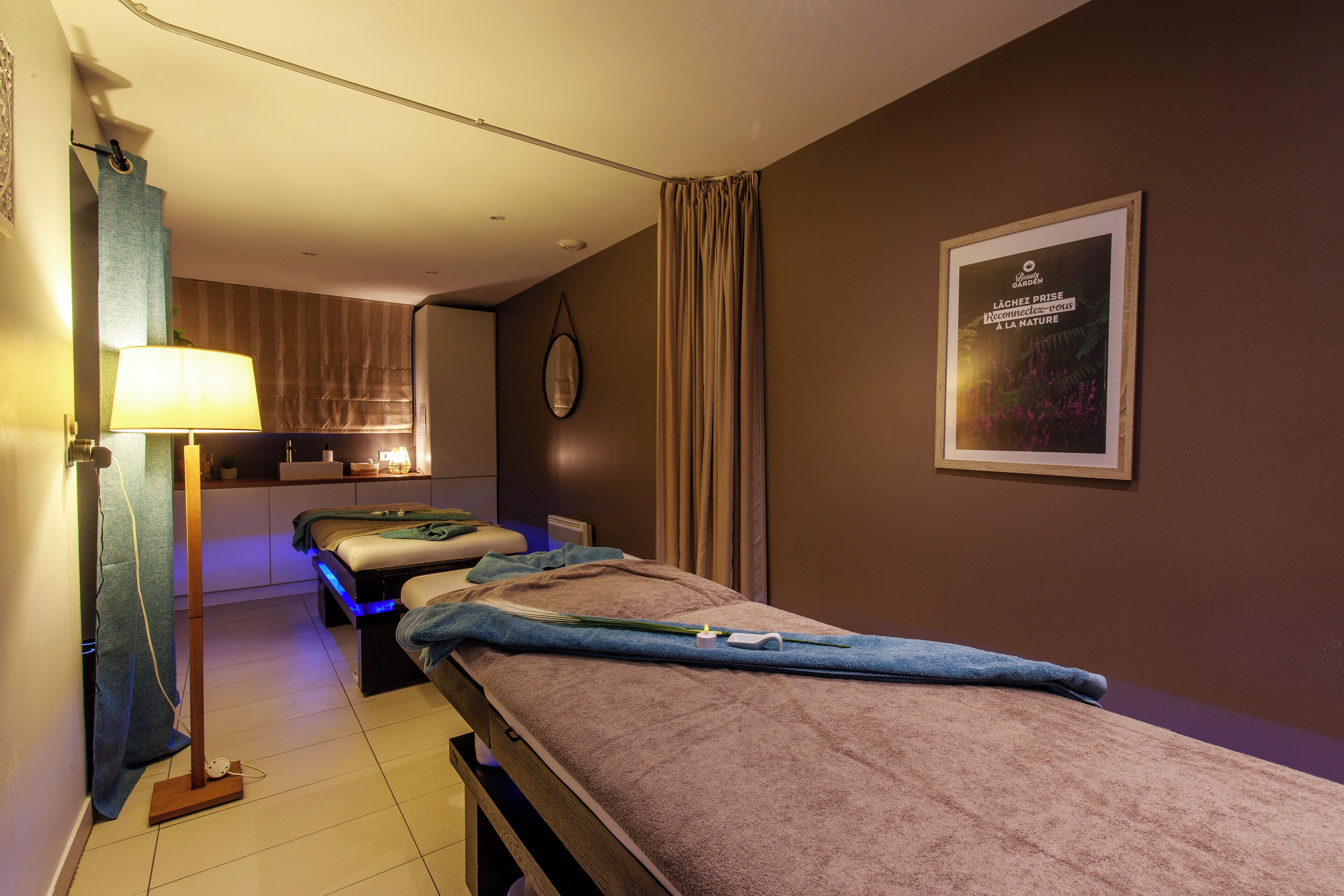 A room with two beds, a bedside table, a lamp, a wall-mounted clock, and a poster.
