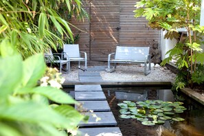 Un giardino tranquillo con uno stagno, due panchine bianche e una statua di Buddha.