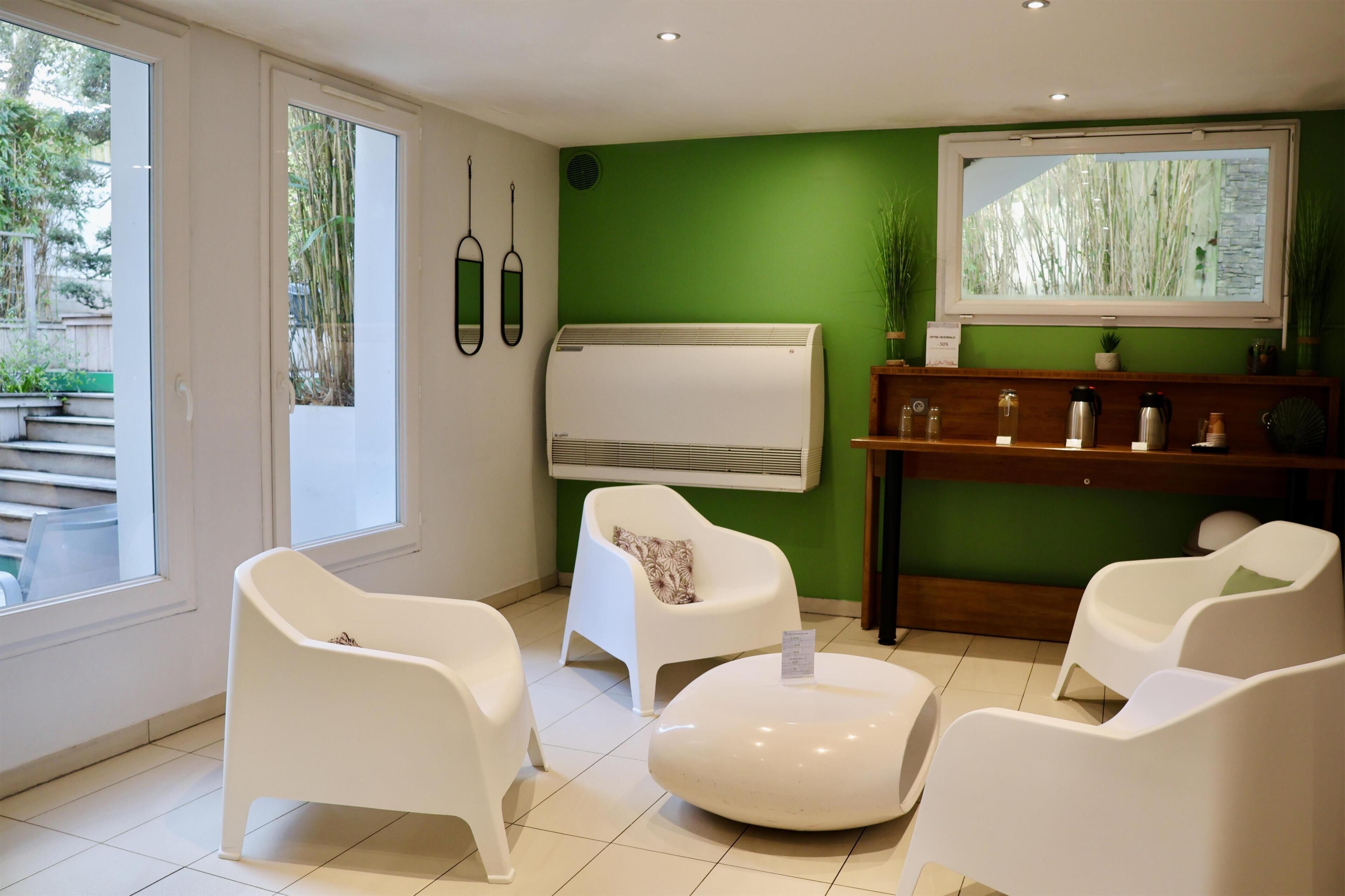 A room with a green wall, white chairs, a white radiator, and a wooden shelf with items.