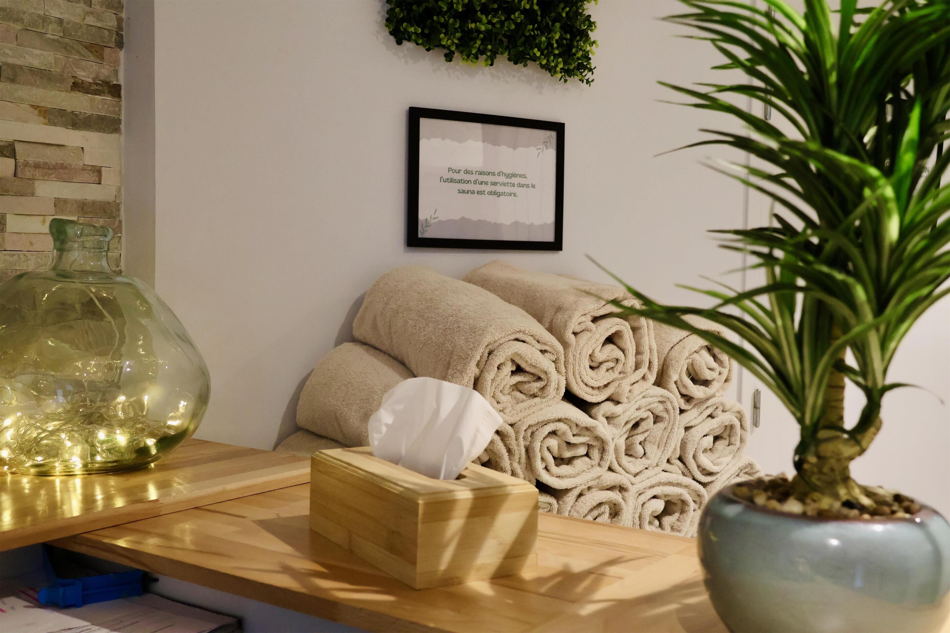 A wooden reception desk with a tissue box, rolled towels, a potted plant, and a framed sign on the wall.