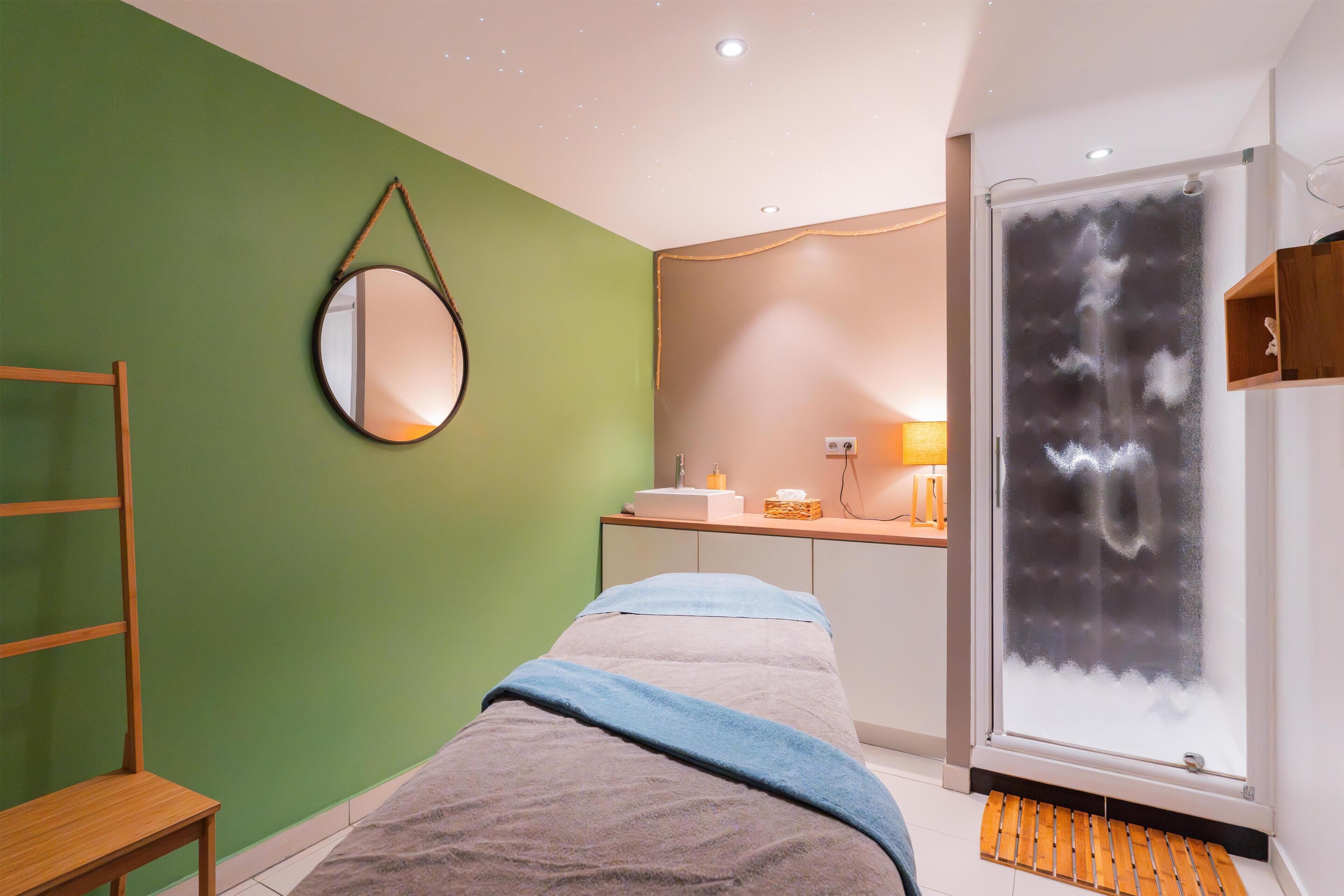 Una habitación con cama, espejo, ventana con vidrio esmerilado, banco de madera y estante con artículos de aseo.