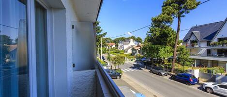 A balcony with a view of a residential street, houses, and parked cars.