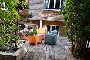Une terrasse en bois, agrémentée de meubles d’extérieur, notamment des chaises et une table, et entourée de plantes et d’arbres.
