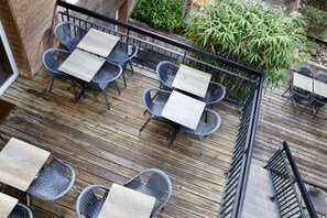 Une terrasse en bois, agrémentée de chaises et de tables en métal, entourée de verdure.