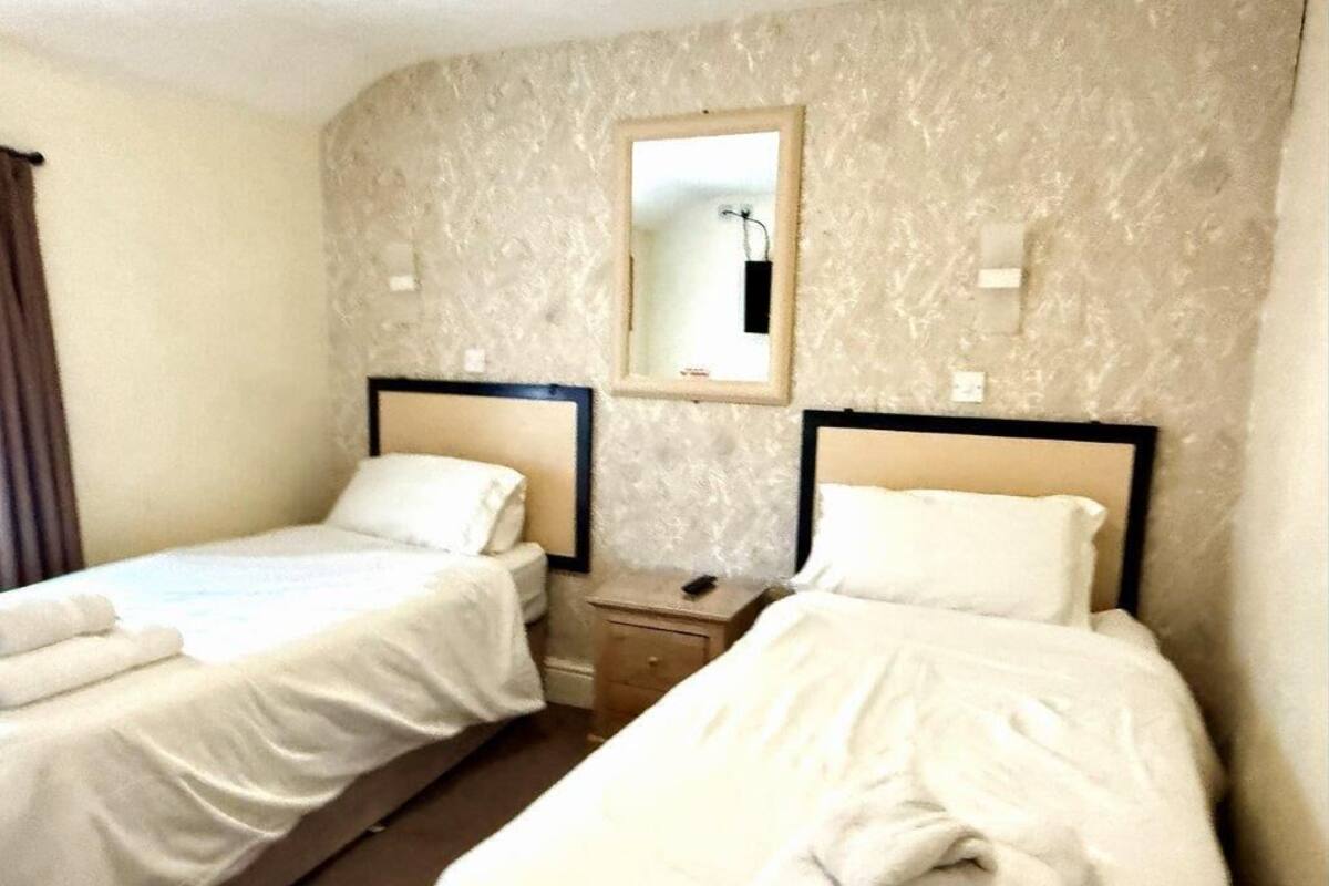 A hotel room with two single beds, a small bedside table, a mirror, and a wall-mounted light fixture.