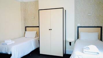 A hotel room with two single beds, a wardrobe, and a bedside table.