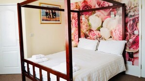A four-poster bed with white linens, a floral wallpaper backdrop, and a framed picture on the wall. -  Deincourt Hotel (Newark)