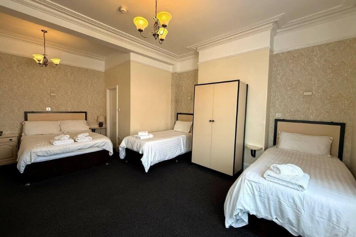 A hotel room with three single beds, a wardrobe, and a chandelier.